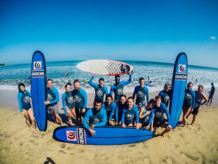 Large group  wearing blue wet suits with blue surf boards on sandy beach with sea in the background