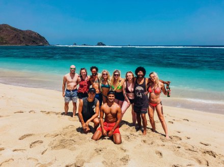 A group photo at the beach in Lombok, Indonesia showing pristine white sand, and two different shades of blue in the ocean
