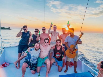 A group of guys on the front deck of the boat while sailing through the Komodo Islands in Indonesia with the bright orange sunset in the background