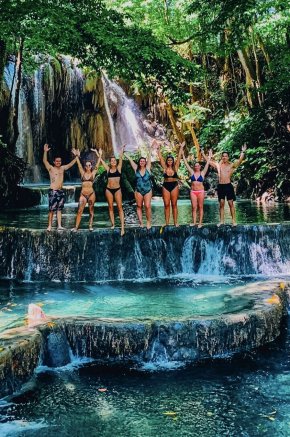 A group standing at the edge of a waterfall tier, showing crystal clear blue waters at Moyo Island, Indonesia 