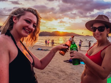 Two girls toasting their beers on the beach at sunset in Phuket, Thailand